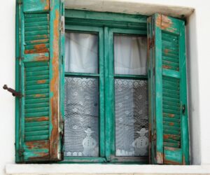 Türkise historische Holzschlagläden mit abgeblätterter Farbe an einem Fenster