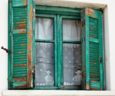 Türkise historische Holzschlagläden mit abgeblätterter Farbe an einem Fenster