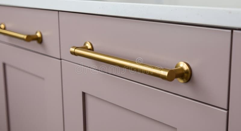 Nahaufnahme eleganter goldener Möbelgriffe an altrosa Küchenfronten.