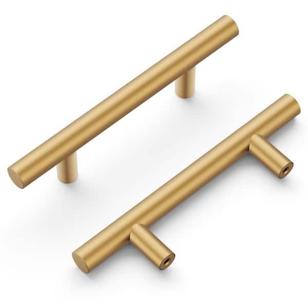 Zwei moderne, goldfarbene Möbelgriffe aus Messing in T-Form vor weißem Hintergrund.